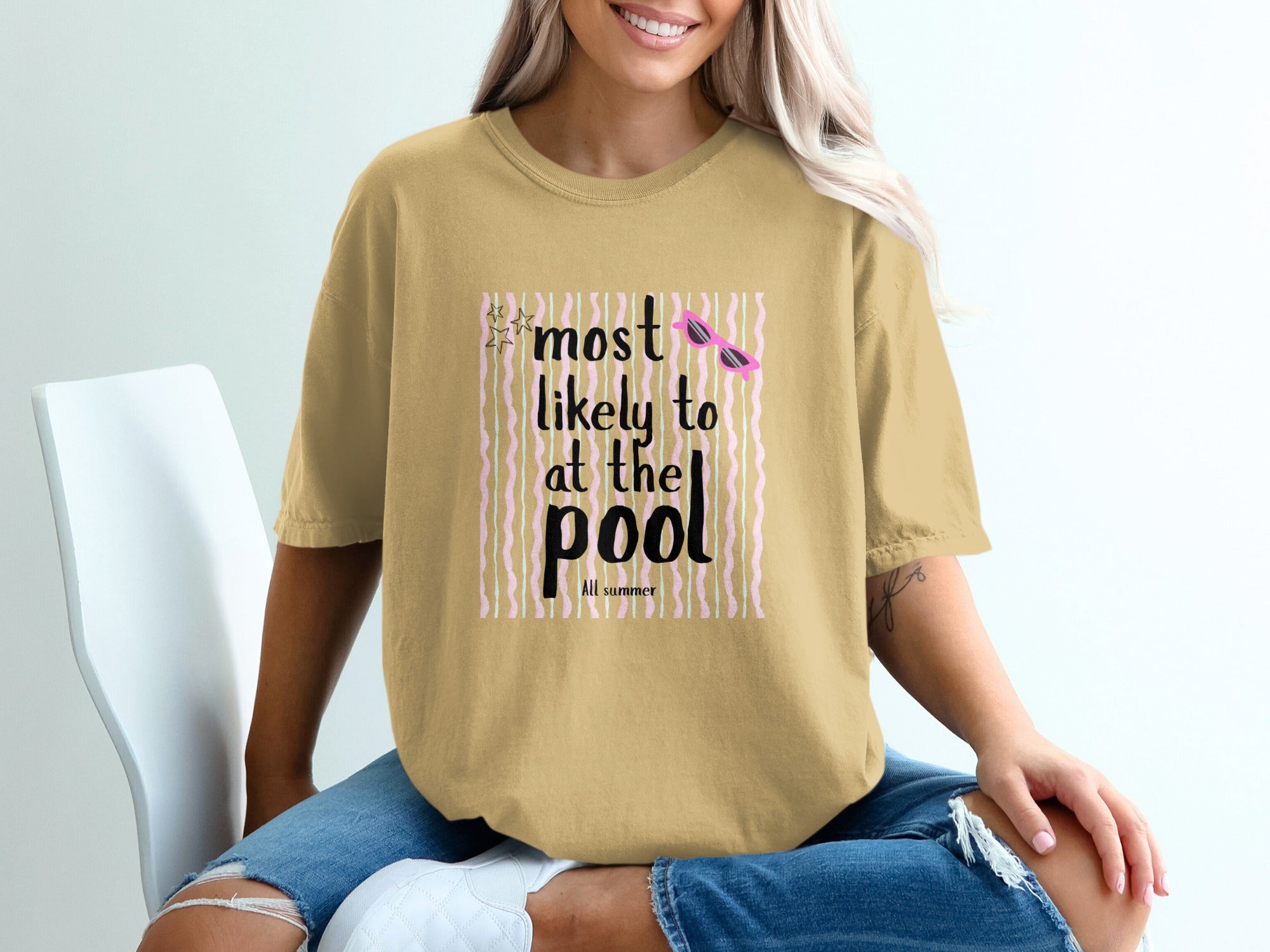 Tan t-shirt with "most likely to at the pool" graphic and pink sunglasses.