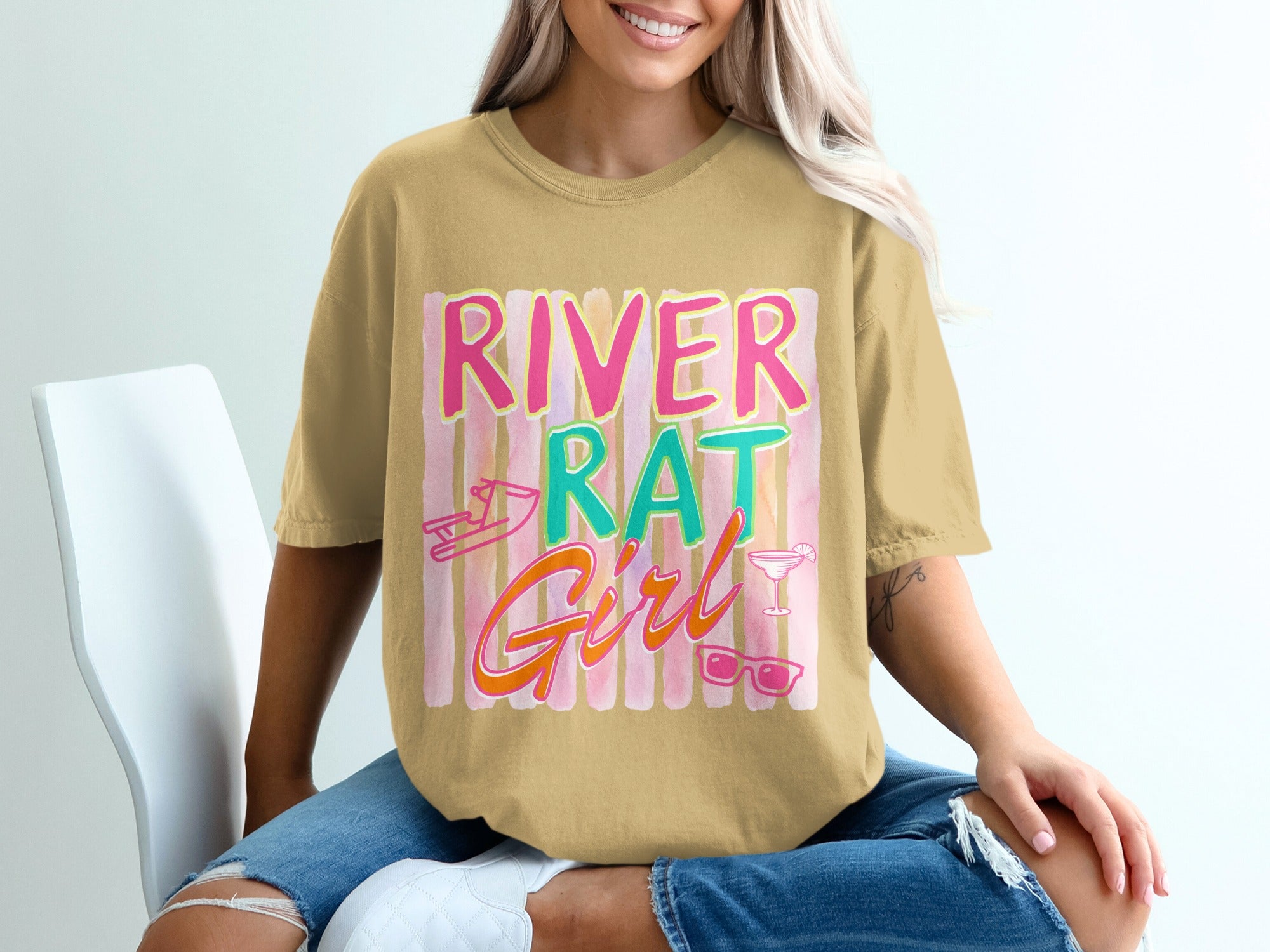 Tan t-shirt with pink and teal text that says "River Rat Girl".