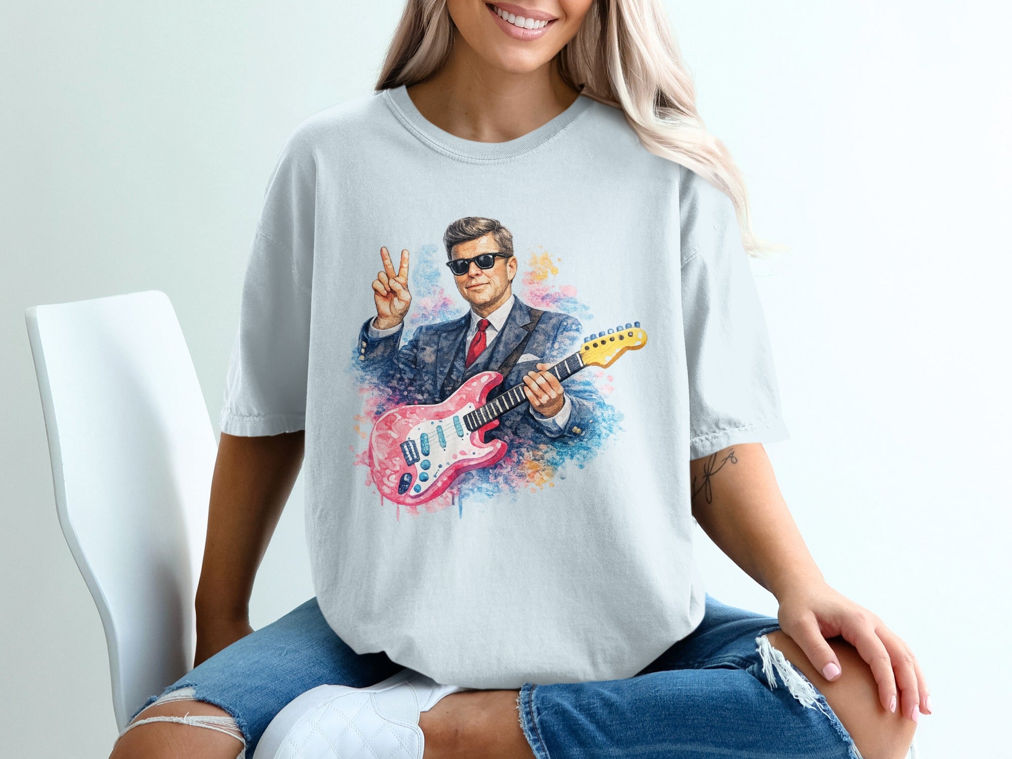 Man in suit and sunglasses plays pink electric guitar, making peace sign.
