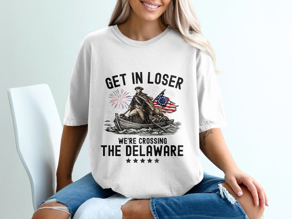 White t-shirt with "Get in loser, we're crossing the Delaware" text and patriotic graphic.