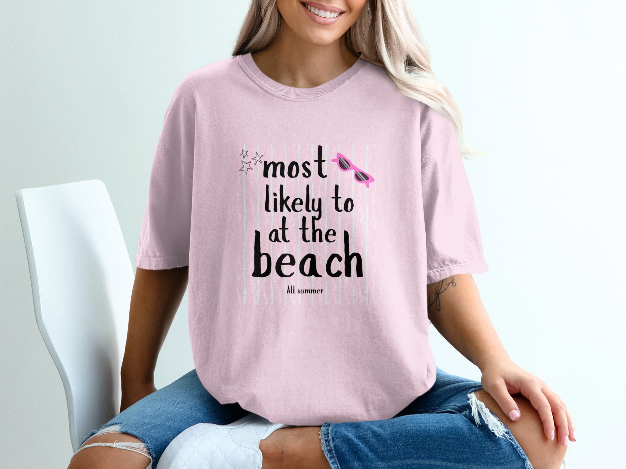 Pink t-shirt with graphic text "most likely to at the beach" and sunglasses.